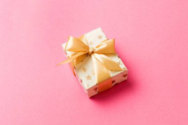 Noel 'i ya da diğer tatil hediyelerini renkli arka planda altın kurdeleli beyaz kağıda sardım. Şimdiki kutu, renkli tabloda hediye süslemesi, kopya alanı ile üst görünüm.