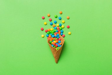 waffle cone full of assorted traditional candies falling out on colored background with copy space. Happy Holidays sale concept.