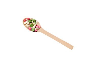 Renkli bir arka planda tahta kaşıkta vitamin kapsülleri. Haplar sağlıklı bir yemek olarak sunuldu. Uyuşturucu, eczane, ilaç veya sağlık hizmetleri kavramı.
