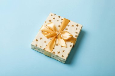 Noel 'i ya da diğer tatil hediyelerini renkli arka planda altın kurdeleli beyaz kağıda sardım. Şimdiki kutu, renkli tabloda hediye süslemesi, kopya alanı ile üst görünüm.