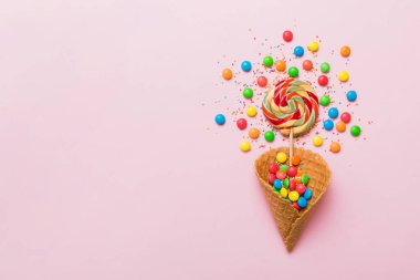 waffle cone full of assorted traditional candies falling out on colored background with copy space. Happy Holidays sale concept.
