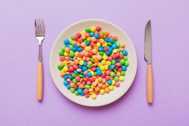 cutlery on table and sweet plate of candy. Health and obesity concept, top view on colored background.