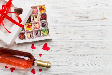 Sevgililer Günü için renkli arka planda bir şişe kırmızı şarap hediye ve çikolatalı. Kalp, hediye kutusuyla şekillendirilmiş çikolatalar fotokopi alanı ile üst görünüm.
