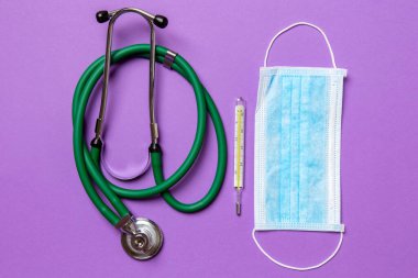 Stetoskop, cıva termometre ve renkli arka planda koruyucu yüz maskesi. Tıbbi ekipman ve sağlık hizmetleri kavramı.
