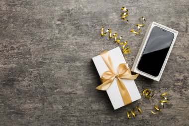 Altın kurdeleli hediye kutusu ve arka planda akıllı telefon, üst manzara. Boş kutu paketleme modeli, tasarımınız için şablon - markalaşma modeli.
