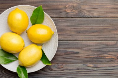 Taze kesilmiş limon ve tüm limonları renkli arka planda yuvarlak tabakta. Yemek ve içecek malzemeleri hazırlanıyor. Sağlıklı beslenme teması üst görünüm kopyalama alanı.