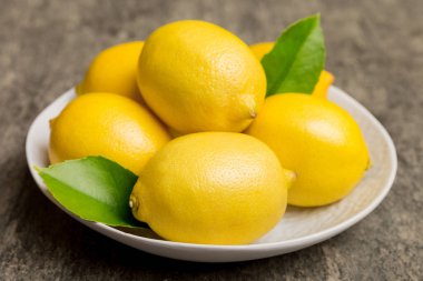 Taze kesilmiş limon ve tüm limonları renkli arka planda yuvarlak tabakta. Yemek ve içecek malzemeleri hazırlanıyor. Sağlıklı beslenme teması üst görünüm kopyalama alanı.