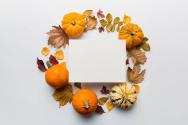 Kağıt boş ve kurumuş yapraklı sonbahar kompozisyonu ve masada balkabağı. Düz konum, üst görünüm, kopyalama alanı.