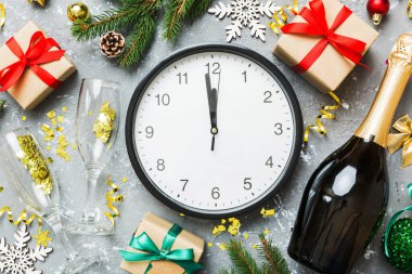 New year celebration concept with a bottle of champagne and two glasses toasting. Christmas gift box, alarm clock and fir tree branch on colored table. Top view Copy space.