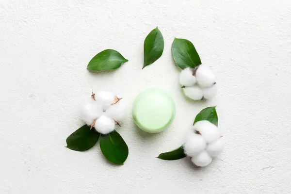 Organic cosmetic products with cotton flower and green leaves on cement background. Flat lay.
