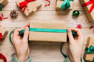 Kadınlar Noel tatili için sürpriz hediyeler hazırlıyor. İş yerinde el aletleri ve manzarayla oturuyor. Renkli masada Noel hediyesini paketleyen kadın..