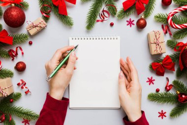 Noel 'i yazmak için bir kadın not defterine Xmas dekorasyonlu renkli arkaplan çiziyor.