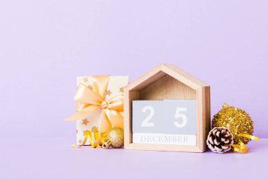 25 december. Christmas composition on colored background with a wooden calendar, with a gift box, toys, bauble copy space.