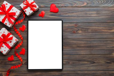 Top view of digital tablet with gift boxes and hearts on colorful background. Tablet with black screen with Holiday decorations gift box top view.