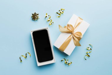 Altın kurdeleli hediye kutusu ve arka planda akıllı telefon, üst manzara. Boş kutu paketleme modeli, tasarımınız için şablon - markalaşma modeli.