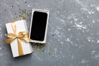 Altın kurdeleli hediye kutusu ve arka planda akıllı telefon, üst manzara. Boş kutu paketleme modeli, tasarımınız için şablon - markalaşma modeli.