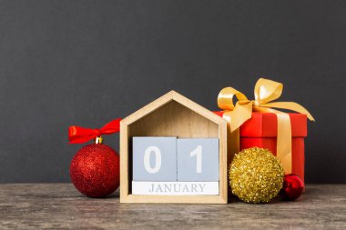 1 january. Christmas composition on colored background with a wooden calendar, with a gift box, toys, bauble copy space.