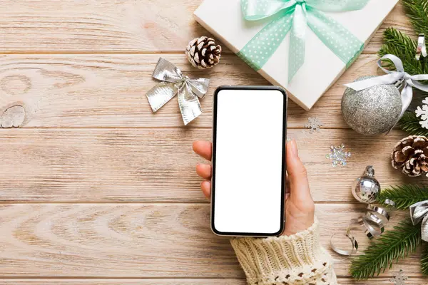 christmas mockup with space for text. christmas advertising, app template. hand holding phone with empty screen on table background. Happy New Year and Xmas Flat lay.