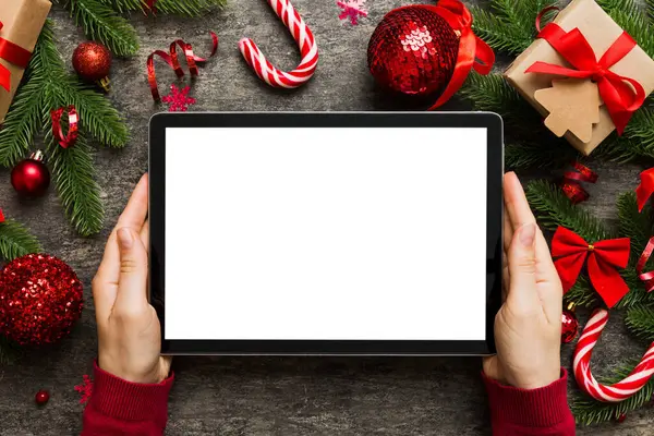 Evden Noel alışverişi, kadın elleri boş beyaz ekranlı tableti tutuyor. Kadın elinde tablet, boş ekran, Noel ağacı ve arka planda hediyeler..