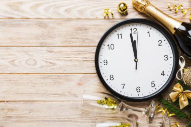 New year celebration concept with a bottle of champagne and two glasses toasting. Christmas gift box, alarm clock and fir tree branch on colored table. Top view Copy space.