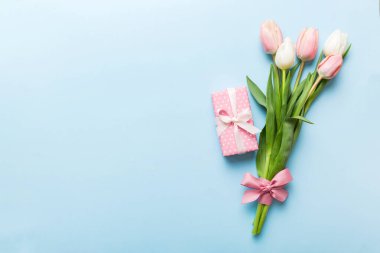 Pembe lale çiçekleri ve hediye ya da renkli masa arkaplanındaki hediye kutusu. Anneler günü, doğum günü, kadınlar günü, kutlama konsepti. Metin üstü görünümü için boşluk.