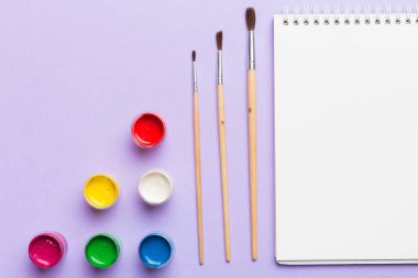 Albüm sayfaları, boyalar, kalemler, renkli arka planda fırçalar. Boşluğu olan üst görünüm. Yaratıcılık için işyeri. ev öğretmenliği kavramı çizimi.