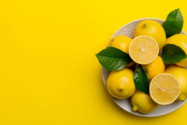 Taze kesilmiş limon ve tüm limonları renkli arka planda yuvarlak tabakta. Yemek ve içecek malzemeleri hazırlanıyor. Sağlıklı beslenme teması üst görünüm kopyalama alanı.