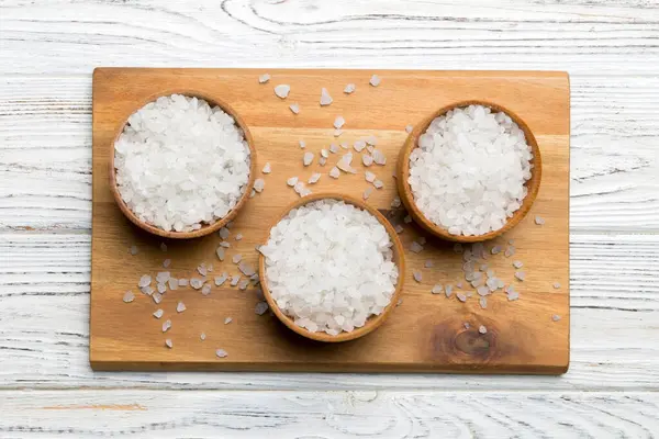 A wooden bowl of salt crystals on a wooden background. Salt in rustic bowls, top view with copy space.