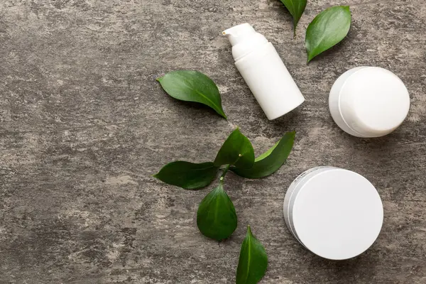 Çimento arka planında yeşil yaprakları olan organik kozmetik ürünler. Uzayı kopyala, düz yat.