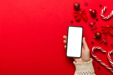 Mesaj atmak için yeri olan bir Noel modeli. Noel reklamı, uygulama şablonu. Masa arkasında boş ekran olan el ele tutuşan telefon. Mutlu yıllar ve Xmas Flat.