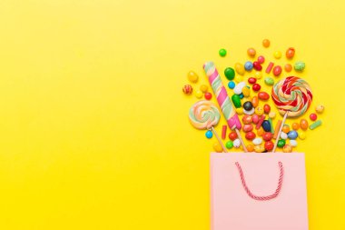 shopping paper gift bag in corner full of assorted traditional candies falling out on colored background with copy space. Happy Holidays sale concept.