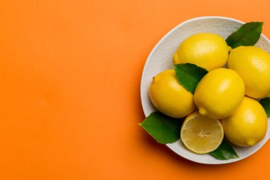 Taze kesilmiş limon ve tüm limonları renkli arka planda yuvarlak tabakta. Yemek ve içecek malzemeleri hazırlanıyor. Sağlıklı beslenme teması üst görünüm kopyalama alanı.