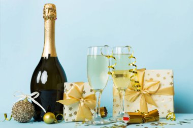 Champagne bottle with confetti, glasses and christmas decor on colored holiday background. Flat lay New Year decorations.