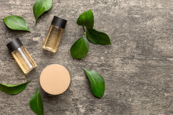 Organic cosmetic products with green leaves on cement background. Copy space, flat lay.