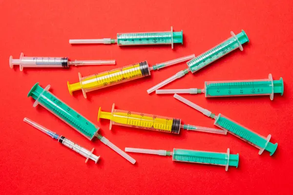Top view of medical syringes with needles at red background with copy space. Injection treatment concept.