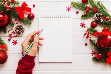 Noel 'i yazmak için bir kadın not defterine Xmas dekorasyonlu renkli arkaplan çiziyor.