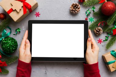 Evden Noel alışverişi, kadın elleri boş beyaz ekranlı tableti tutuyor. Kadın elinde tablet, boş ekran, Noel ağacı ve arka planda hediyeler..