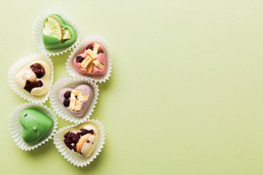 chocolate sweets in the form of a heart with fruits and nuts on a colored background. top view with space for text, holiday concept.