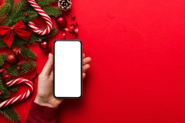 Mesaj atmak için yeri olan bir Noel modeli. Noel reklamı, uygulama şablonu. Masa arkasında boş ekran olan el ele tutuşan telefon. Mutlu yıllar ve Xmas Flat.