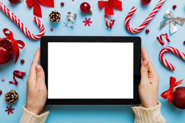 Evden Noel alışverişi, kadın elleri boş beyaz ekranlı tableti tutuyor. Kadın elinde tablet, boş ekran, Noel ağacı ve arka planda hediyeler..