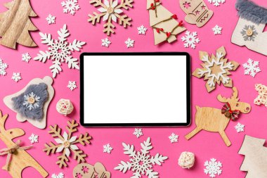 Tatil süslemeleri ve oyuncaklardan yapılmış pembe arka planda dijital tabletin en üst görüntüsü. Noel süsü konsepti.