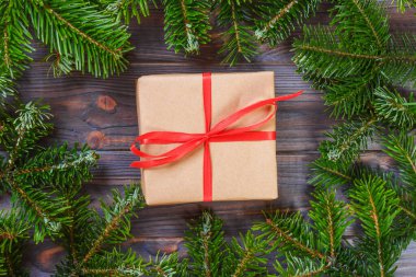 Çam dalları köpekler ile yapılmış bir çerçeve içinde koyu ahşap arka plan üzerinde kırmızı kurdele ile Noel hediyeleri. Düz yatıyordu stili.