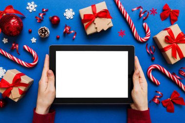 Evden Noel alışverişi, kadın elleri boş beyaz ekranlı tableti tutuyor. Kadın elinde tablet, boş ekran, Noel ağacı ve arka planda hediyeler..