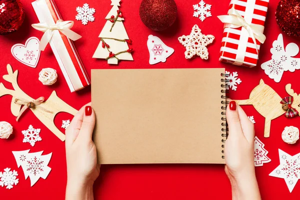 Kadın elinin rengarenk arka planda notlar aldığına dair üst görünüm. Yeni yıl süslemeleri ve oyuncakları. Noel zamanı konsepti.