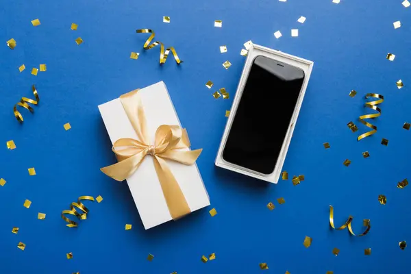 Opened gift box with gold ribbon and smartphone on color background, top view. Blank open box packaging mockup , Template for your design - branding mockup.