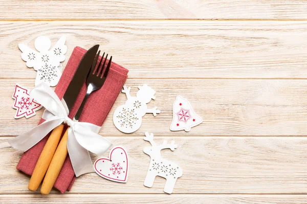 Top view of New Year dinner on wooden background. Festive cutlery on napkin with christmas decorations and toys. Family holiday concept with copy space.