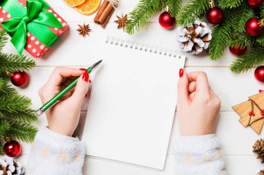 Ahşap Noel arka planında bir not defterine kadın el yazısının üst görüntüsü. Firavun ağacı ve şenlikli süsler. Dilek listesi. Yeni yıl konsepti.