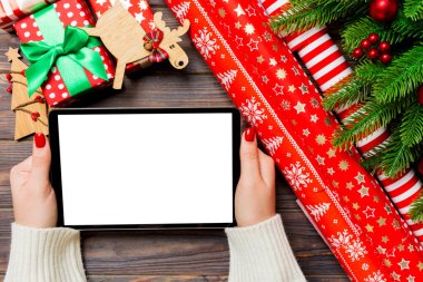 Kadın ellerinin, köknar ağacı ve şenlikli süslemelerden yapılmış ahşap Noel arka planında bir tablet taşıdığı en üst görüntü. Yeni yıl tatili konsepti. Model.