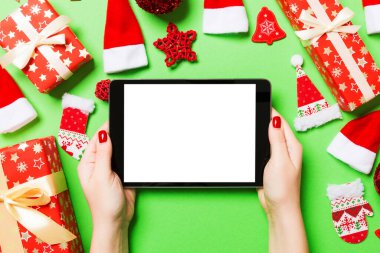 Elinde tabletle Noel süslemelerinden yapılmış yeşil arka planda gezen kadının üst görüntüsü. Yeni yıl tatili konsepti. Model.