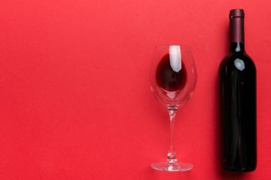 Bir bardak kırmızı şarap ve renkli masada bir şişe. Düz konum, üst görünüm kopyalama alanı.
